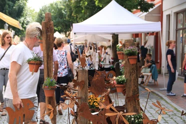 Kunst & Handwerkermarkt.JPG Belebter Kunst- und Handwerkermarkt mit Besuchern, weißen Ständen und rostiger Gartendeko.