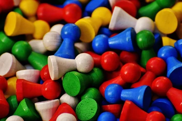 Zahlreiche bunte Holzspielfiguren in Rot, Blau, Grün, Gelb und Naturholz liegen dicht beieinander.