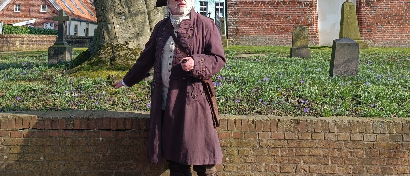 Hafenmeister Quirinus in Greetsiel Hafenmeister Quirinus im historischen Gewand mit Dreispitz vor der alten Backsteinkirche.