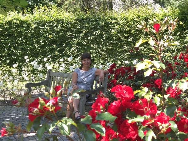 Speckenbütteler Park (c) Mailin Knoke (5)_WEB.jpg Lächelnde Frau auf einer Bank im Rosengarten im Gesundheitspark Speckenbüttel