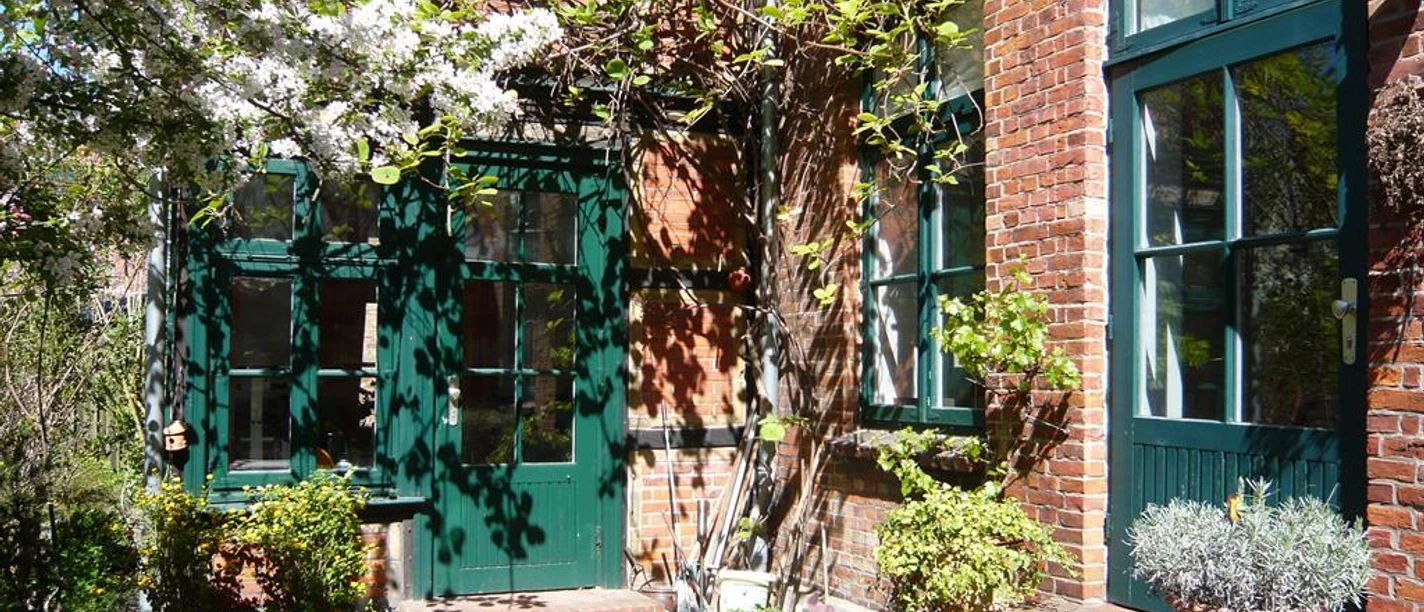 Ferienwohnung Lünecastle Innenhof Grüne Türen an einer Backsteinfassade mit blühendem Baum und Topfpflanzen im sonnigen Innenhof.