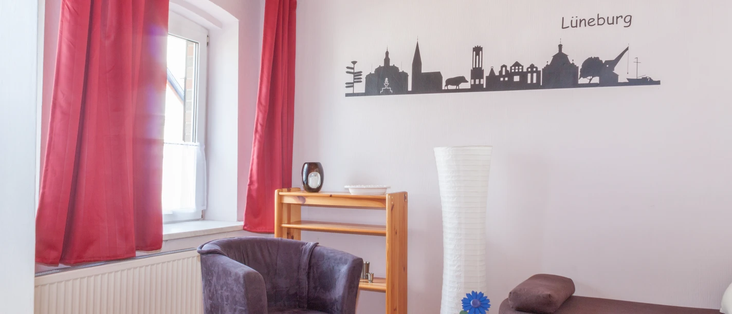 Ferienwohnung Wedemeyer Wohnzimmer Wohnbereich mit Sessel, Sofa, Holztisch, roten Vorhängen und einer Lüneburg-Wandsilhouette.