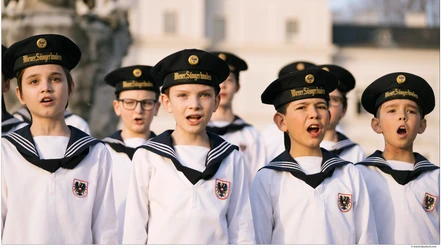 Wiener Sängerknaben in Matrosenuniformen singen vor hellem Gebäude.