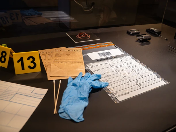 Serienkiller - Die True Crime Ausstellung Forensische Utensilien wie Beweismittelbeutel, Handschuhe und Markierungen auf einem Tisch.