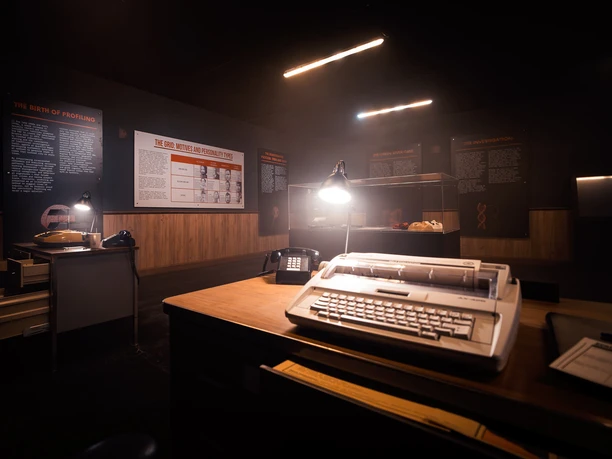 Serial Killer - The True Crime Exhibition Darkened exhibition room with old desks, lamps, telephones and information boards