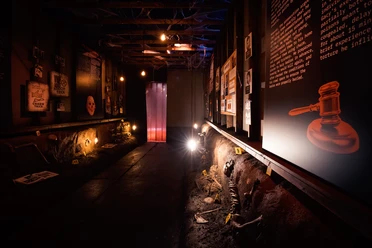 Serial Killer - The True Crime Exhibition Dark exhibition room with information boards, illuminated finds and marked skeleton fragments.
