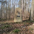 Domeier Gedenkstein Steinerner Gedenkstein mit Porträtmedaillon und Plakette auf laubbedecktem Waldboden.
