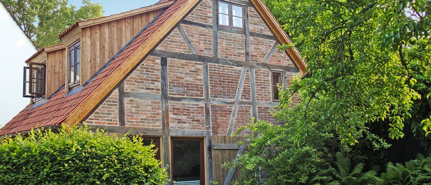Ferienwohnungen Stift Benedikt Außenansicht Rotes Backsteinfachwerkhaus mit Ziegeldach, Holzanbau und Terrasse, umgeben von grünen Büschen.