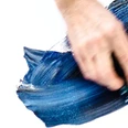 Eine Hand malt mit Hilfe eines Schwammes mit blauer Farbe auf weißen Untergrund.