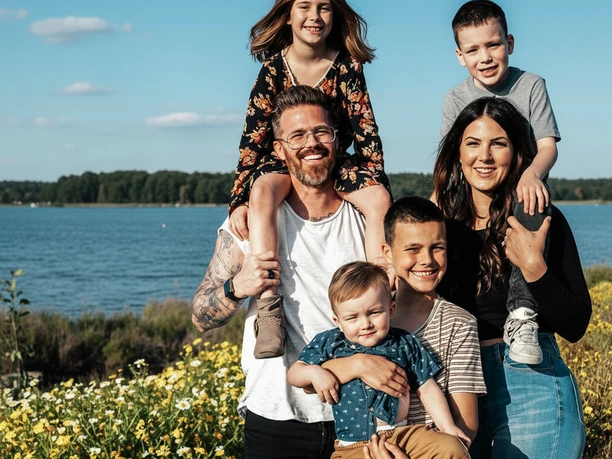OfflineZeit-Familienzeit.png Eine lachende Familie mit vier Kindern steht vor gelben Blumen am Ufer des Steinhuder Meeres.