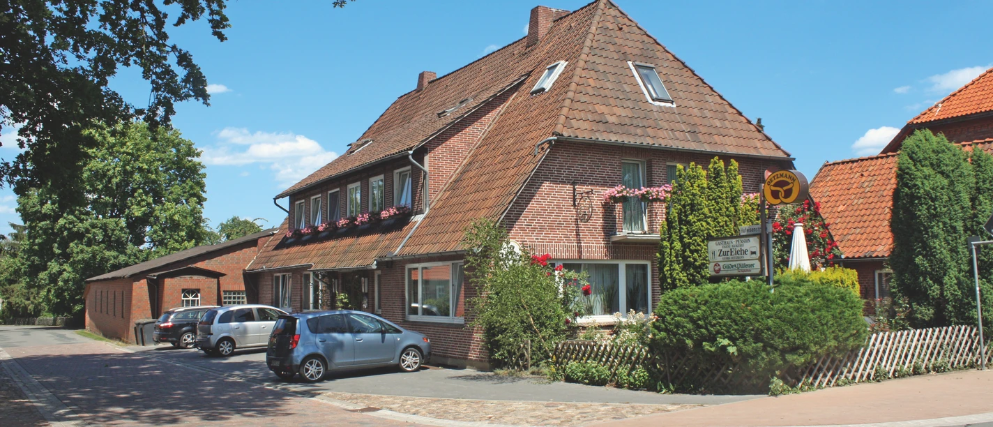 Gasthaus, Pension & Bäckerei "Zur Eiche" Außenansicht Rotes Backsteingebäude des Gasthauses Zur Eiche an einer Straßenecke mit parkenden Autos.