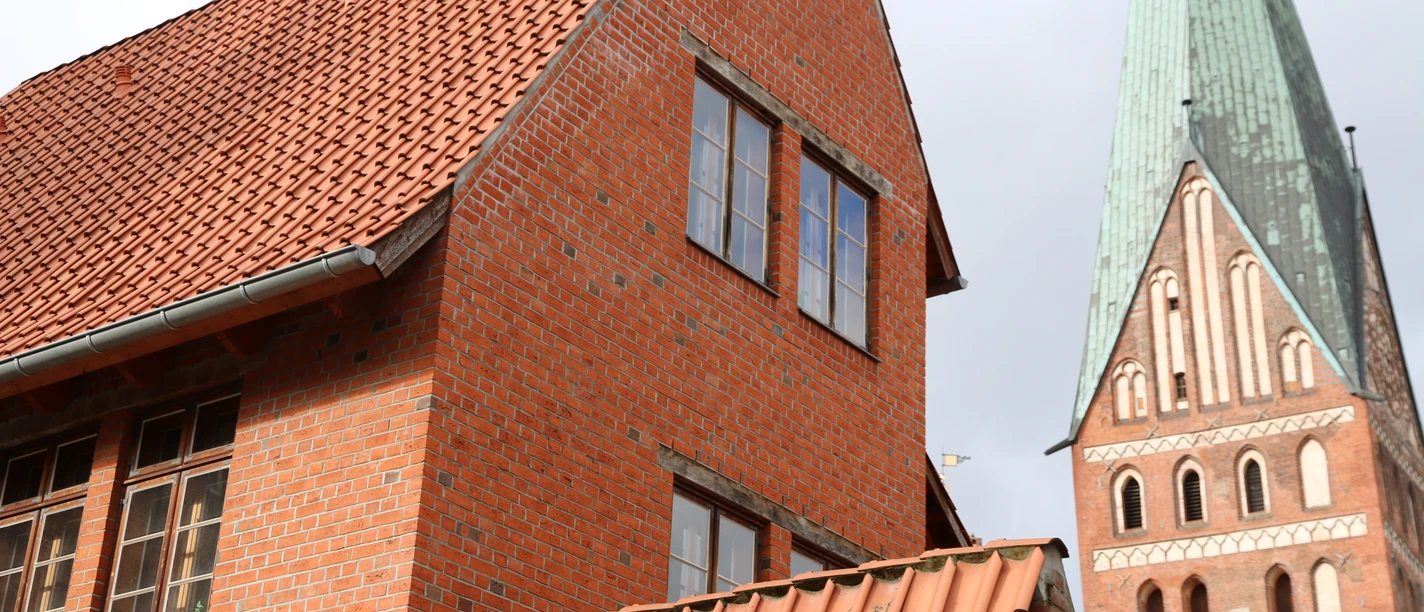 Gästehaus am Wasserturm Außenansicht Rotes Backsteinhaus im Vordergrund, dahinter ein historischer Kirchturm mit grüner Spitze.
