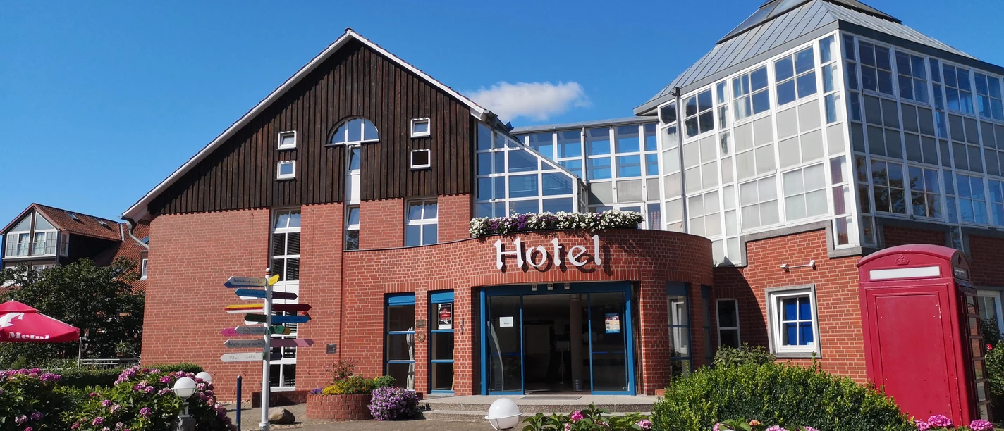 Heide Hotel Reinstorf Außenansicht Außenansicht des Heide Hotel Reinstorf mit roter Backsteinfassade, blauem Himmel und blühenden Hortensien.