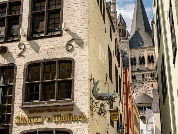 Historische Altstadt von Köln Enge Kopfsteinpflastergasse mit historischen Fassaden und Blick auf den Turm einer großen Kirche.