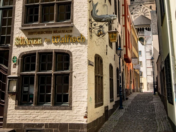 Old town of Cologne Narrow cobblestone alley with historic facades and a view of the tower of a large church.