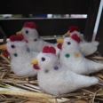 Gefilzte Hühner - MoorIZ Fünf handgemachte, weiße Filzhühner mit bunten Punkten und roten Kämmen sitzen auf trockenem Stroh.