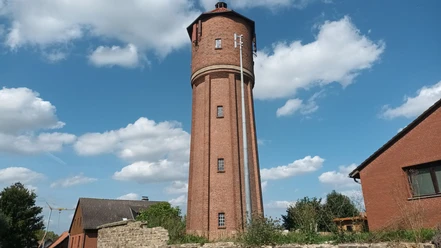 Wasserturm (5)_HD_16zu9.jpg Hoher Wasserturm aus rotem Backstein vor strahlend blauem Himmel mit weißen Wolken.