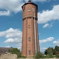 Wasserturm (5)_HD_16zu9.jpg Hoher Wasserturm aus rotem Backstein vor strahlend blauem Himmel mit weißen Wolken.