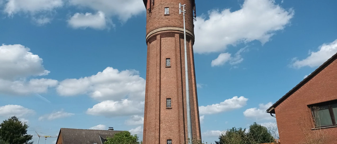 Wasserturm (5)_HD_16zu9.jpg Hoher Wasserturm aus rotem Backstein vor strahlend blauem Himmel mit weißen Wolken.