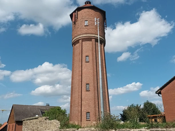 Wasserturm (5)_HD_16zu9.jpg Hoher Wasserturm aus rotem Backstein vor strahlend blauem Himmel mit weißen Wolken.