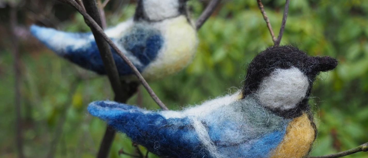 gefilzte Meisen - MoorIZ Zwei handgefilzte Blaumeisen sitzen auf feinen Zweigen in der grünen Natur.