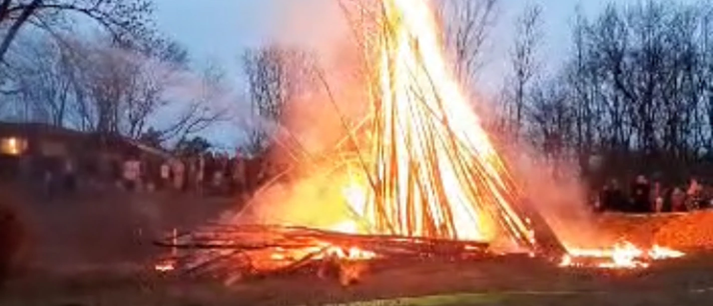 Osterfeuer in Einbeck Ein Osterfeuer brennt auf einer Wiese in der Dämmerung, im Hintergrund stehen Menschen.