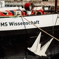 Ein schwimmendes Science Center Bug der MS Wissenschaft mit weißem Anker, Seilen und technischer Ausrüstung am Deck.