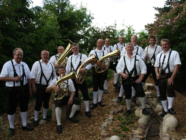 IMG_2030-kl.jpg Musiker in Lederhosen posieren mit Blasinstrumenten in einem Garten.
