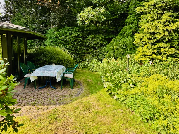 Apartment Hof Düker - Außenbereich Sitzgruppe unter Pavillon im grünen Garten mit Rasen und dichtem Bewuchs