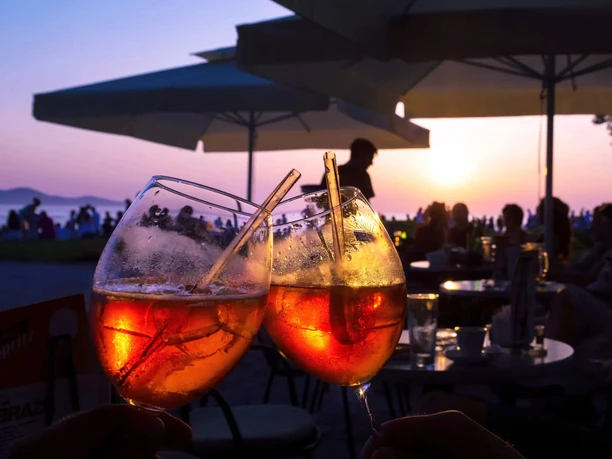 Two Aperol glasses Two glasses of Aperol toast in the evening light, surrounded by seats and gentle silhouettes.