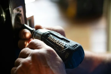 Gemeinsames Reparieren im Repair Café Zwei Hände reparieren mit einem Akkuschrauber der Marke Makita ein Schloss an einer dunklen Tür.