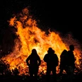 Osterfeuer-Burlage.jpg Silhouetten von Menschen betrachten nachts ein großes, hell loderndes Osterfeuer.