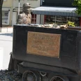 Bergmann_HD_16zu9.JPG Bronzestatue eines Bergmanns hinter einer schwarzen Lore mit Gedenktafel am Marktplatz.