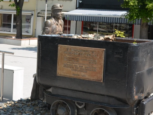 Bergmann_HD_16zu9.JPG Bronzestatue eines Bergmanns hinter einer schwarzen Lore mit Gedenktafel am Marktplatz.