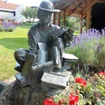 Lesende_HD_16zu9.jpg Bronzestatue Die Lesende auf Büchern in einem Garten mit Lavendel und roten Rosen.