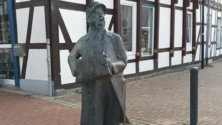 Seppchen Muthig_HD_16zu9.jpg Bronzestatue von Seppchen Muthig mit Akkordeon vor einem Fachwerkhaus in Salzgitter.