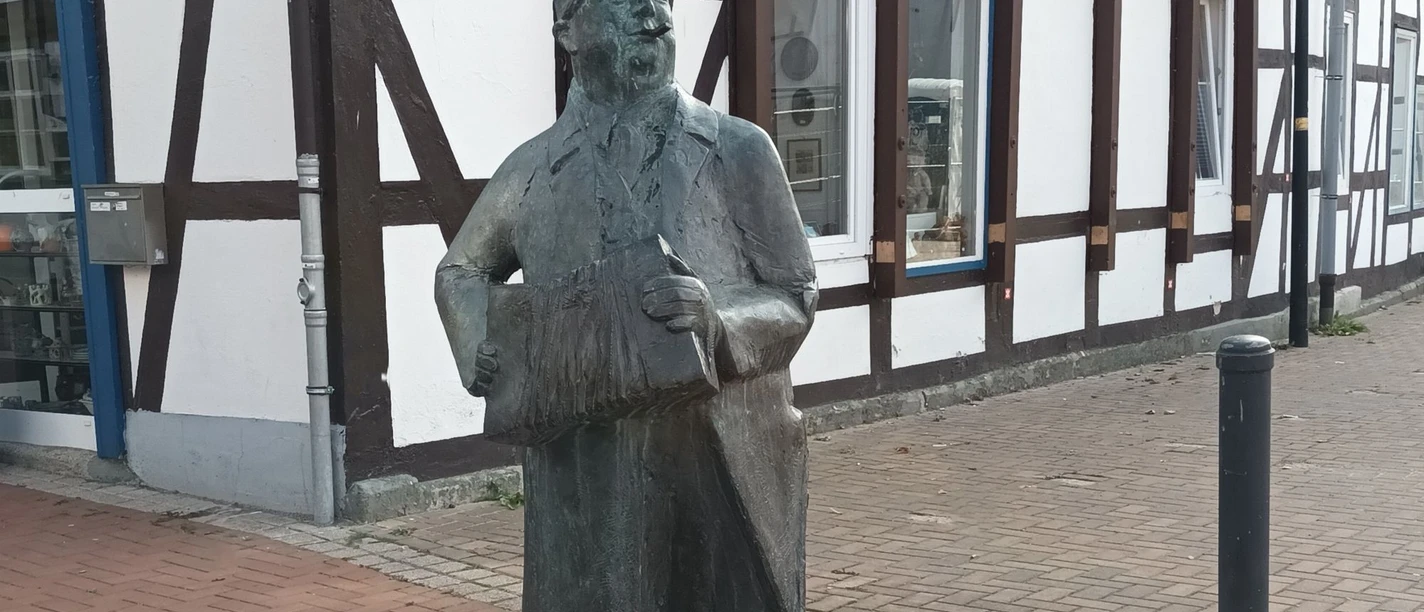 Seppchen Muthig_HD_16zu9.jpg Bronzestatue von Seppchen Muthig mit Akkordeon vor einem Fachwerkhaus in Salzgitter.