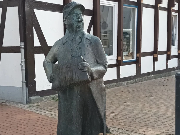 Seppchen Muthig_HD_16zu9.jpg Bronzestatue von Seppchen Muthig mit Akkordeon vor einem Fachwerkhaus in Salzgitter.