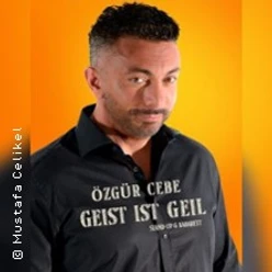 Mann vor orangefarbenem Hintergrund mit schwarzem Hemd und weißem Aufdruck.