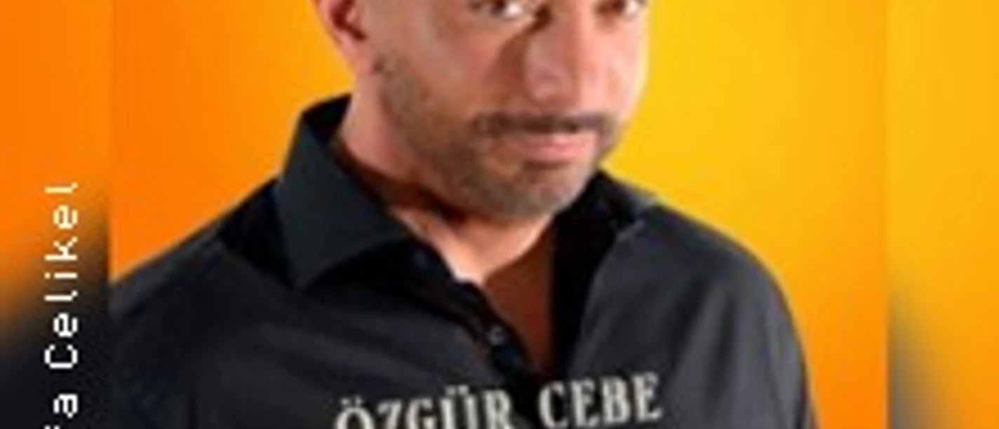 Mann vor orangefarbenem Hintergrund mit schwarzem Hemd und weißem Aufdruck.