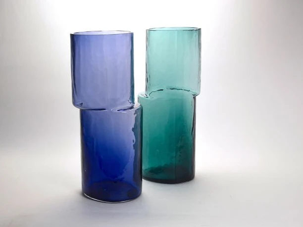 Glass works by Cornelius Reer Two cylindrical glass objects in blue and green with offset shapes on a light background