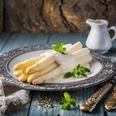 Spargelbuffetessen Frischer weißer Spargel mit Sauce Hollandaise auf einem Teller, garniert mit grünen Blättern.