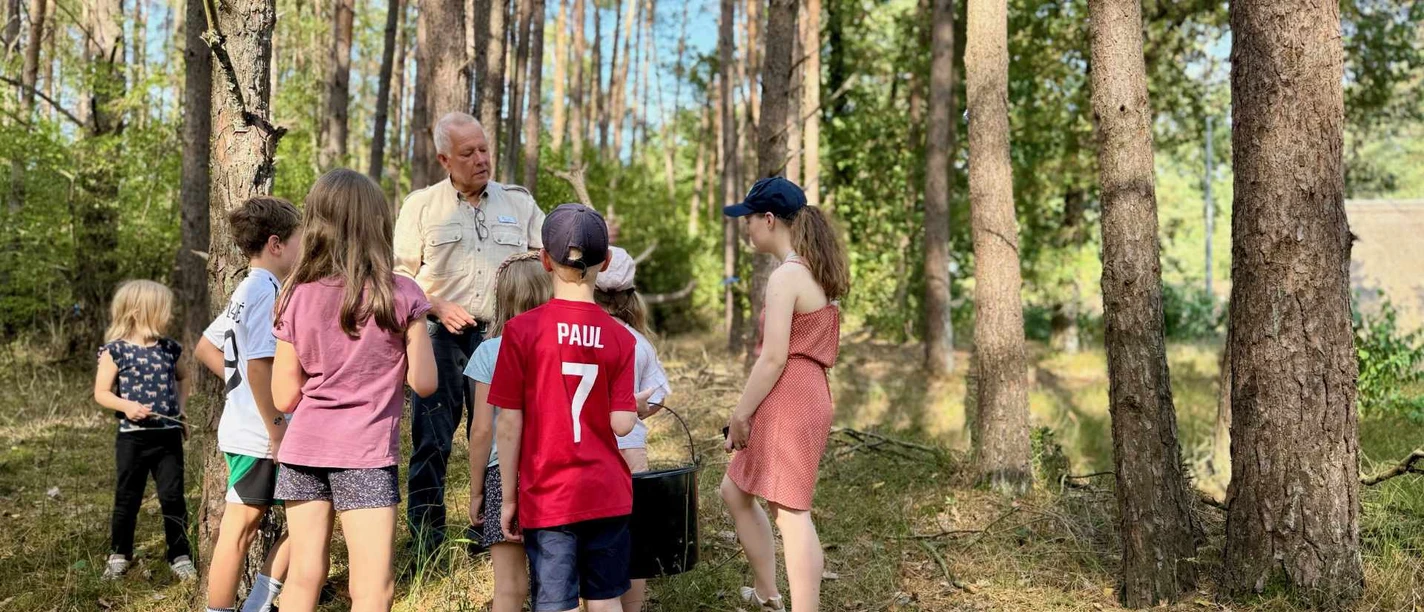 wald-detektive-bispingen (2).jpg Kinder stehen im Wald und lauschen aufmerksam den Erklärungen eines Naturführers.