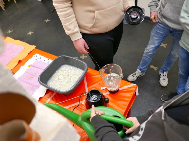 Kreatives Papierschöpfen Kinder und Erwachsene schöpfen Papier. Mehrere Personen hantieren mit Behältern an einem Tisch.