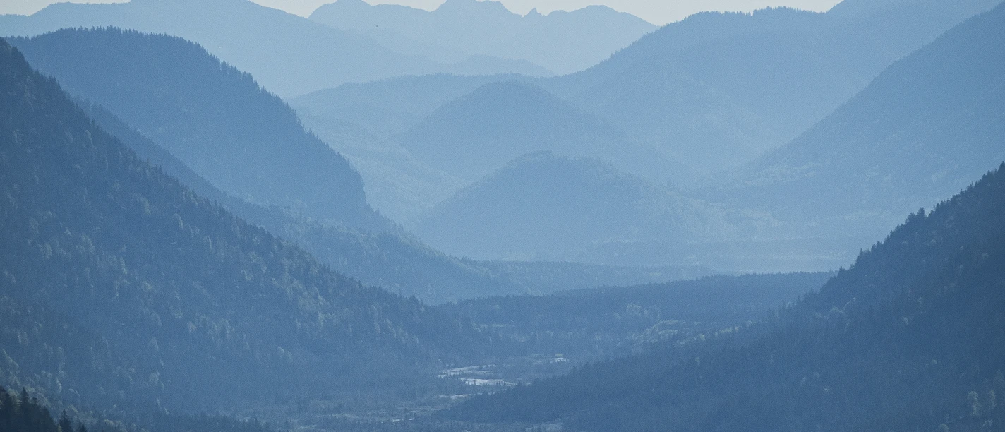 Krepelschrofen Maxhütte Blick über bewaldete Berghänge auf eine weite, neblige Talebene mit sanften Gipfeln