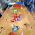Origamitag Bunte Origami-Figuren wie Schmetterlinge und Kraniche auf einem Holztisch während einer Bastelaktion.