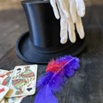 Zauberwerkstatt Zylinder mit weißen Handschuhen, Spielkarten und bunten Federn auf dunklem Holz.