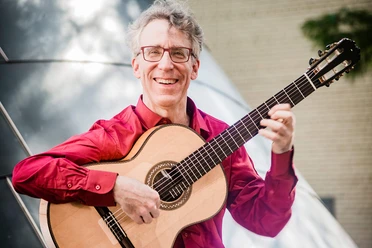 Eliot Fisk-2-(c) Keitaro Yoshioka.jpg Lachender Eliot Fisk in rotem Hemd an seiner Gitarre