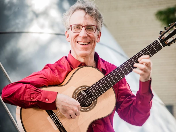 Eliot Fisk-2-(c) Keitaro Yoshioka.jpg Lachender Eliot Fisk in rotem Hemd an seiner Gitarre