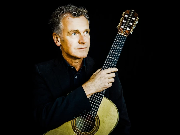 Augustin Wiedemann-by Christine Lang.jpeg Augustin Wiedemann mit Gitarre in der Hand vor schwarzem Hintergrund